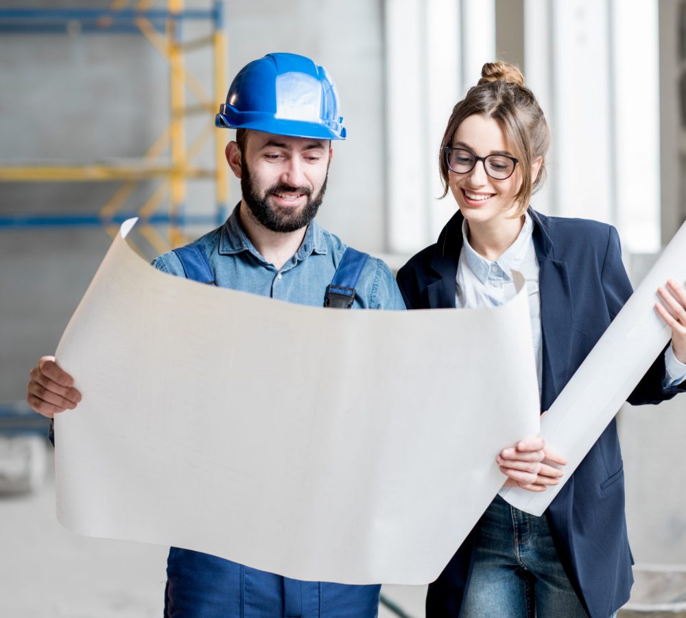 Foreman expertising the structure with businesswoman holding a blueprints at the construction site indoors